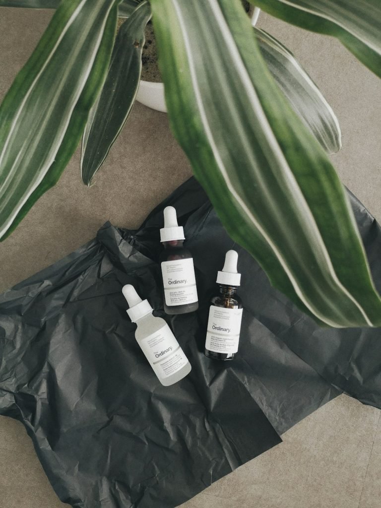 The Ordinary skincare product shot on a black background with a plant.